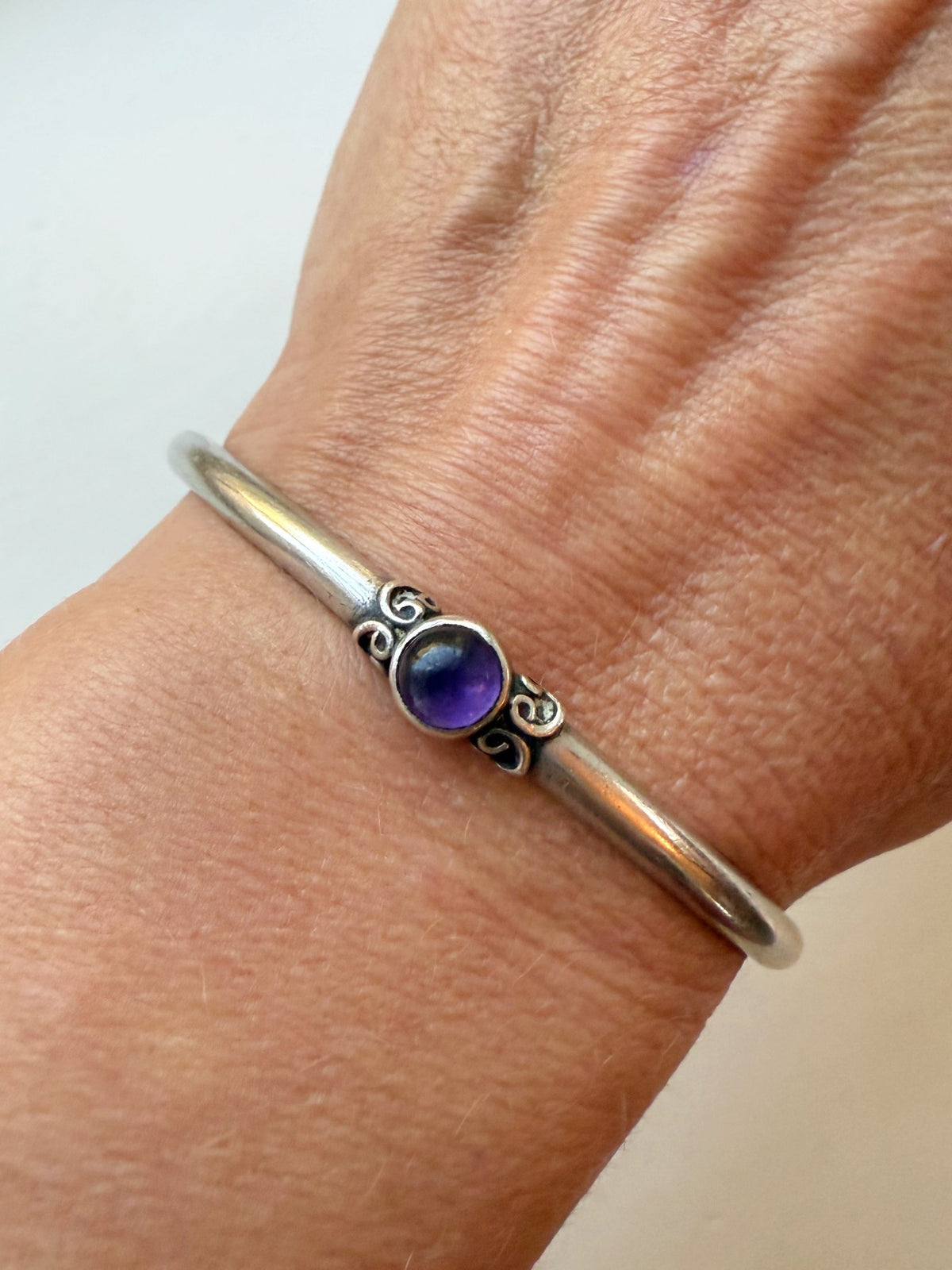 Silver bracelet with a purple gemstone on a wrist against a neutral background