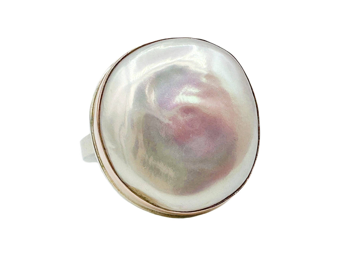 Close up view of the pearl showing subtle flashes of green, violet and pink and the organic shape that's like dollops of cloud.