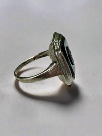 Side view of a white gold ring with a black stone on a white surface