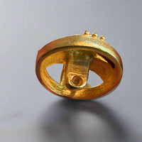 Gold decorative button held between fingers with more buttons in the background.