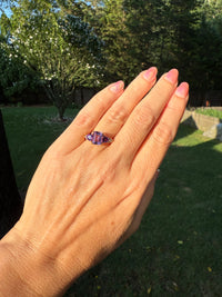 Hand wearing a purple gemstone ring with a blurred natural background