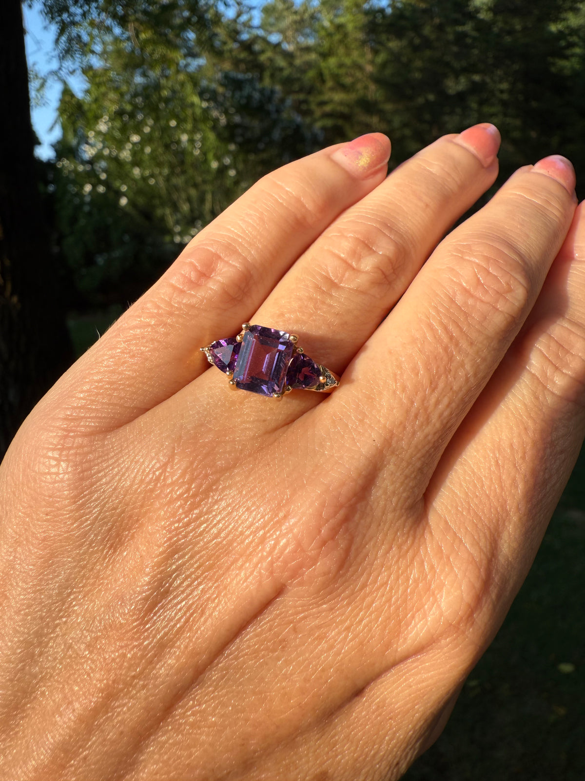 Hand wearing a purple amethyst ring with a blurred natural background