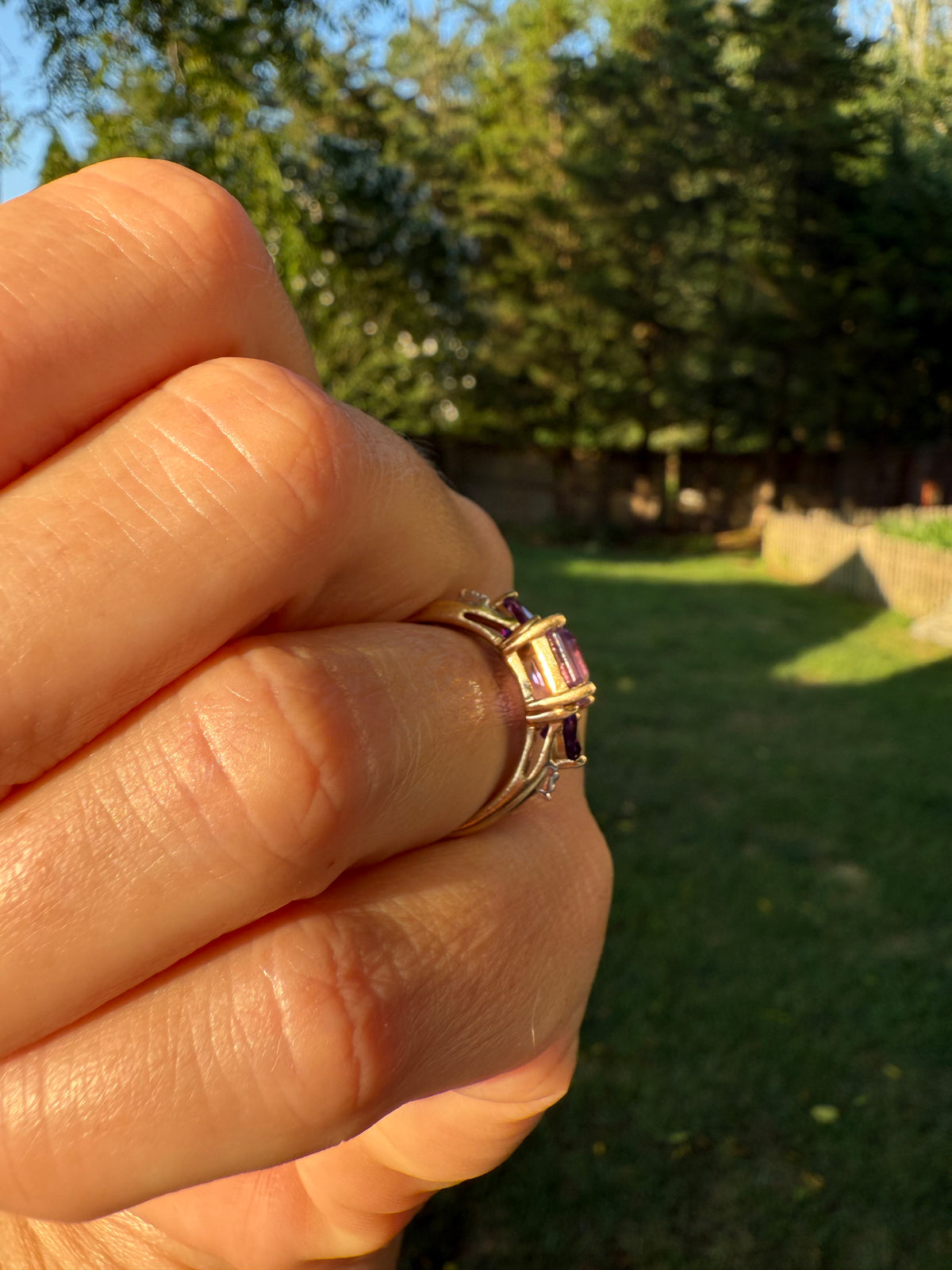 Hand wearing a ring with a gemstone against a blurred outdoor background