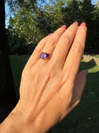 Hand wearing a purple ring with a blurred outdoor background