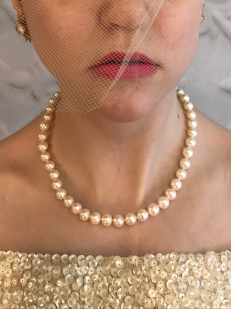 Model wearing pearl necklace and a decorative headpiece against a textured white background