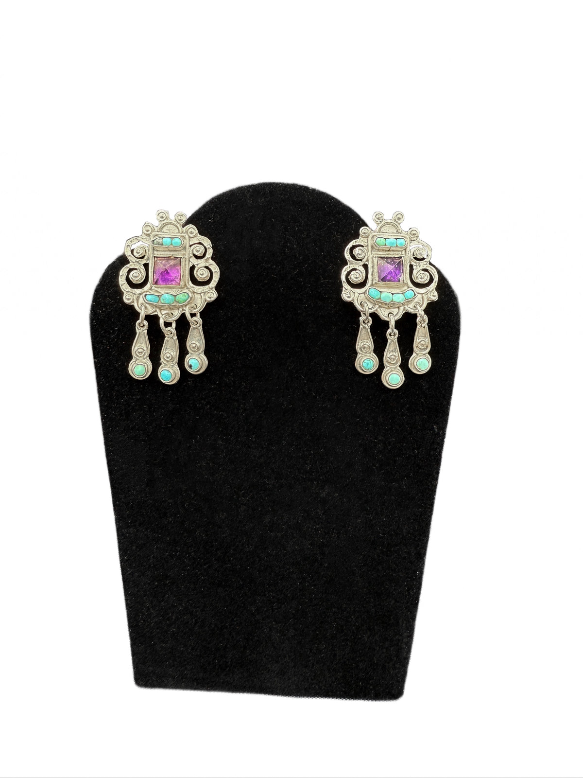 Pair of ornate Matl 925 amethyst and turquoise earrings on a black stand with a white background